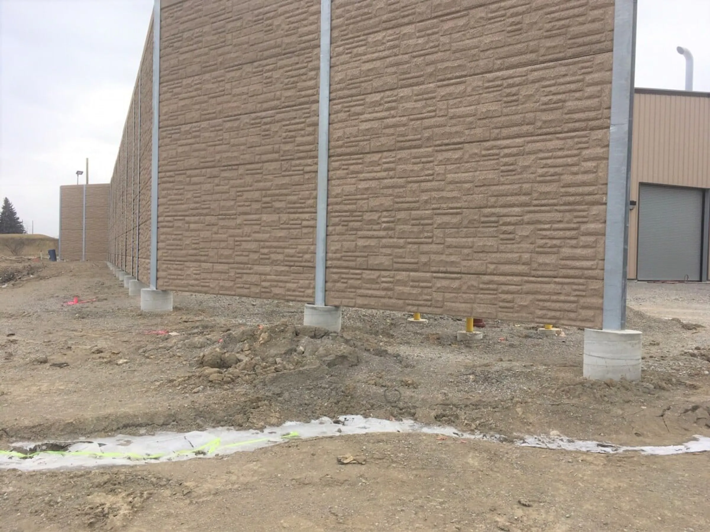 Brown stone-patterned noise wall under construction beside the landfill gas processing building