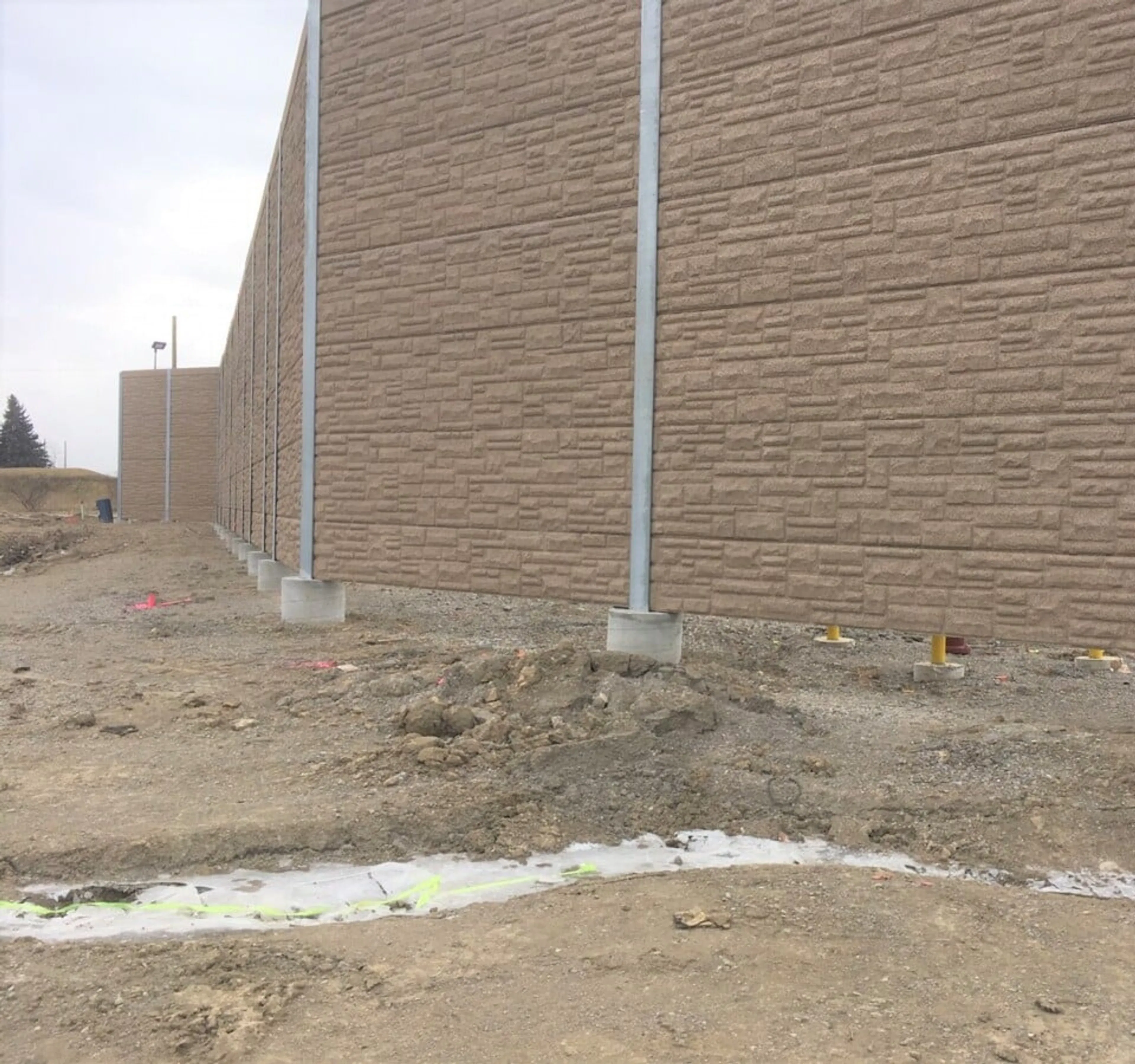 Brown stone-patterned noise wall under construction beside the landfill gas processing building