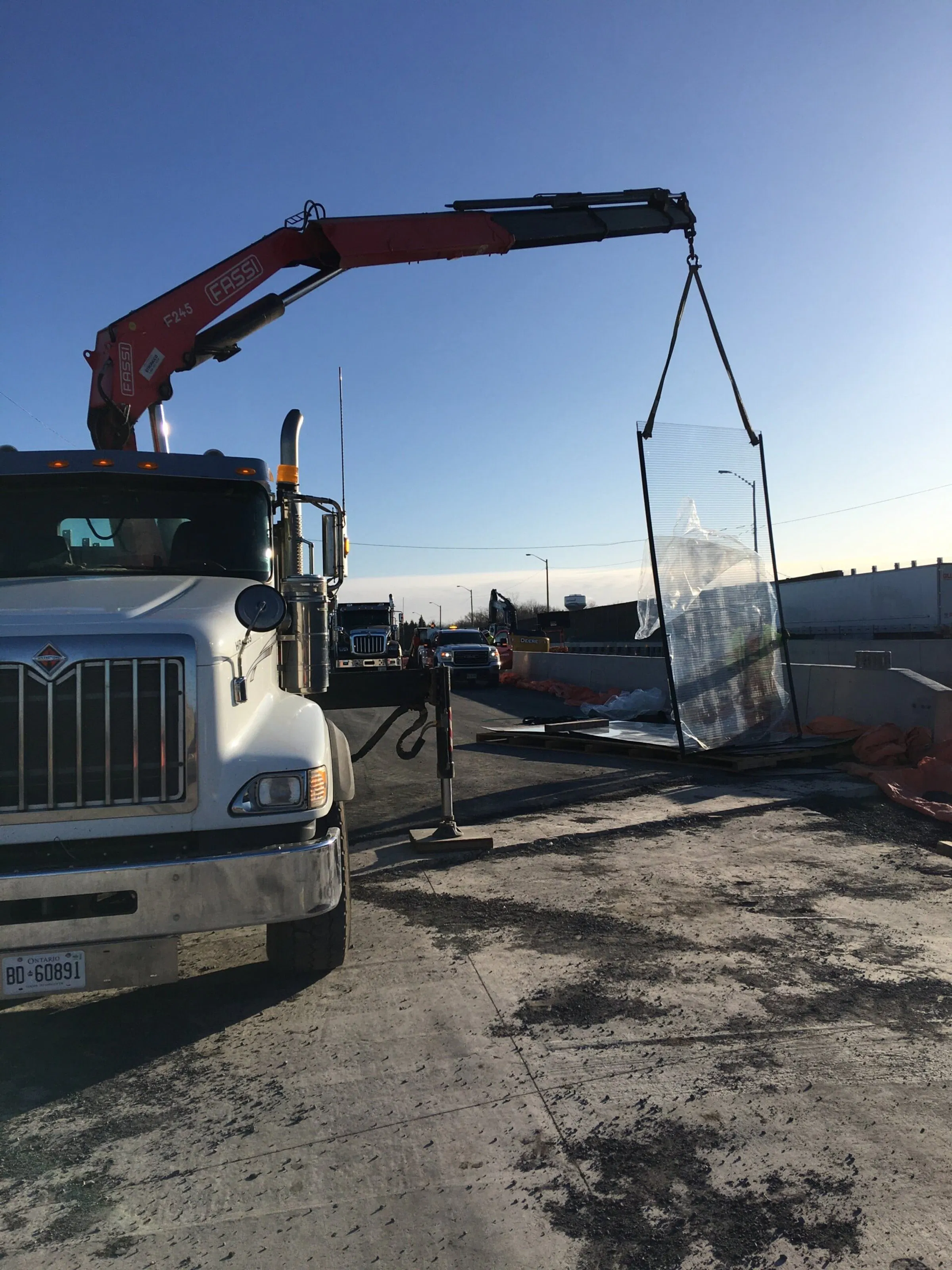 Truck-mounted crane lifting a wrapped transparent noise panel at the Highway 401 overpass work zone