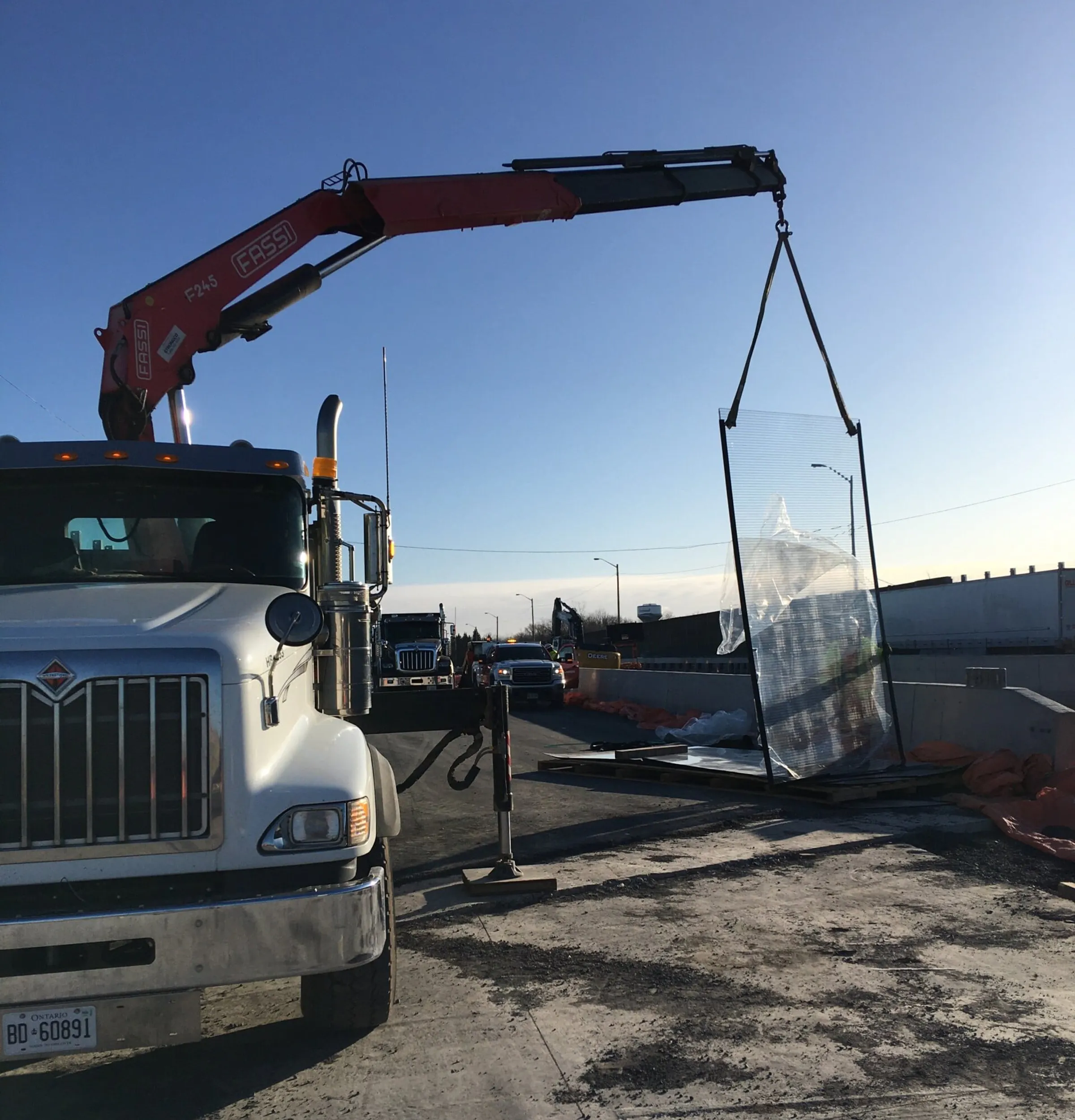 Truck-mounted crane lifting a wrapped transparent noise panel at the Highway 401 overpass work zone
