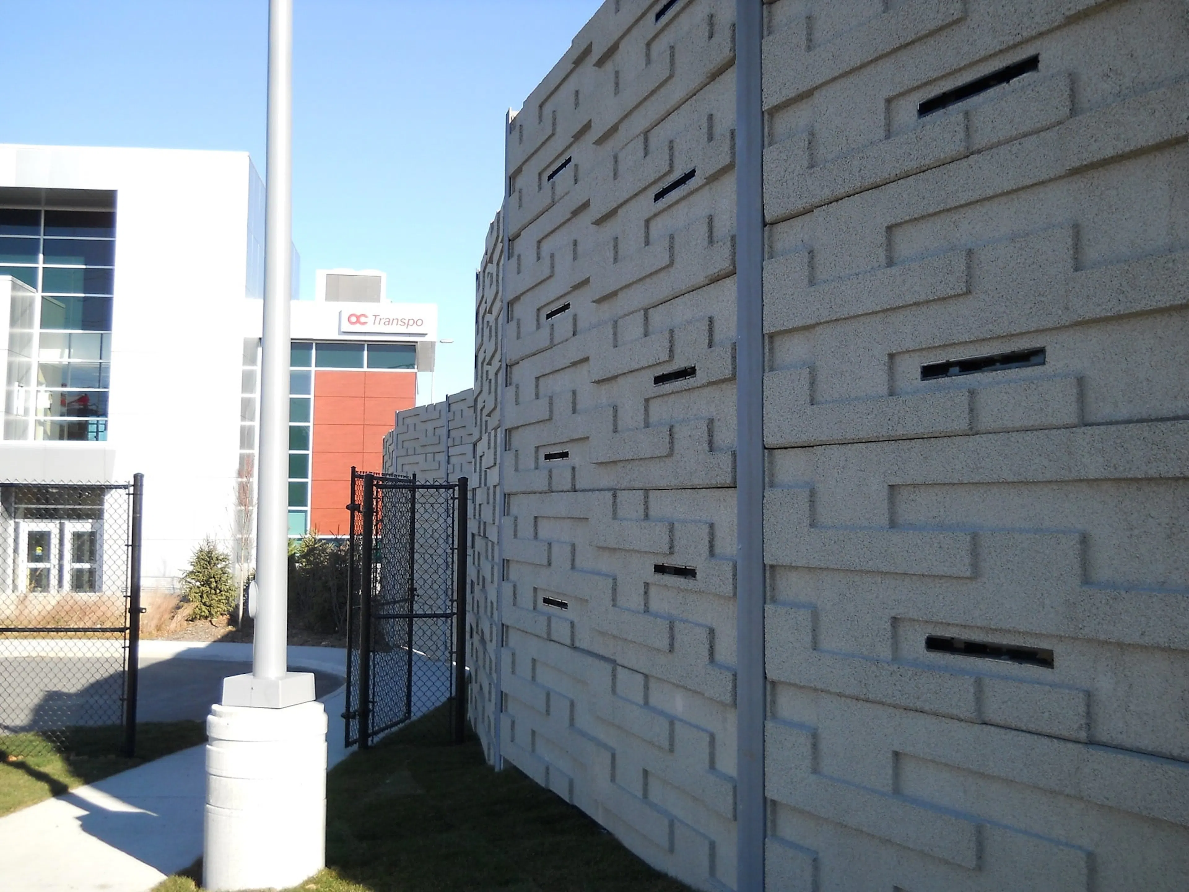 Staggered block noise wall with recessed slots angling away beside the OC Transpo facility