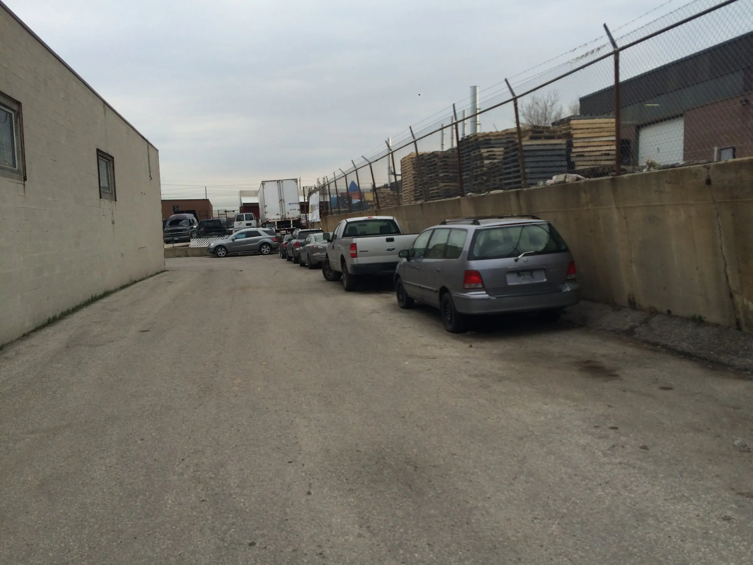 Narrow service lane at the Smokey Manufacturing plant before construction, cars parked below the failing concrete retaining wall