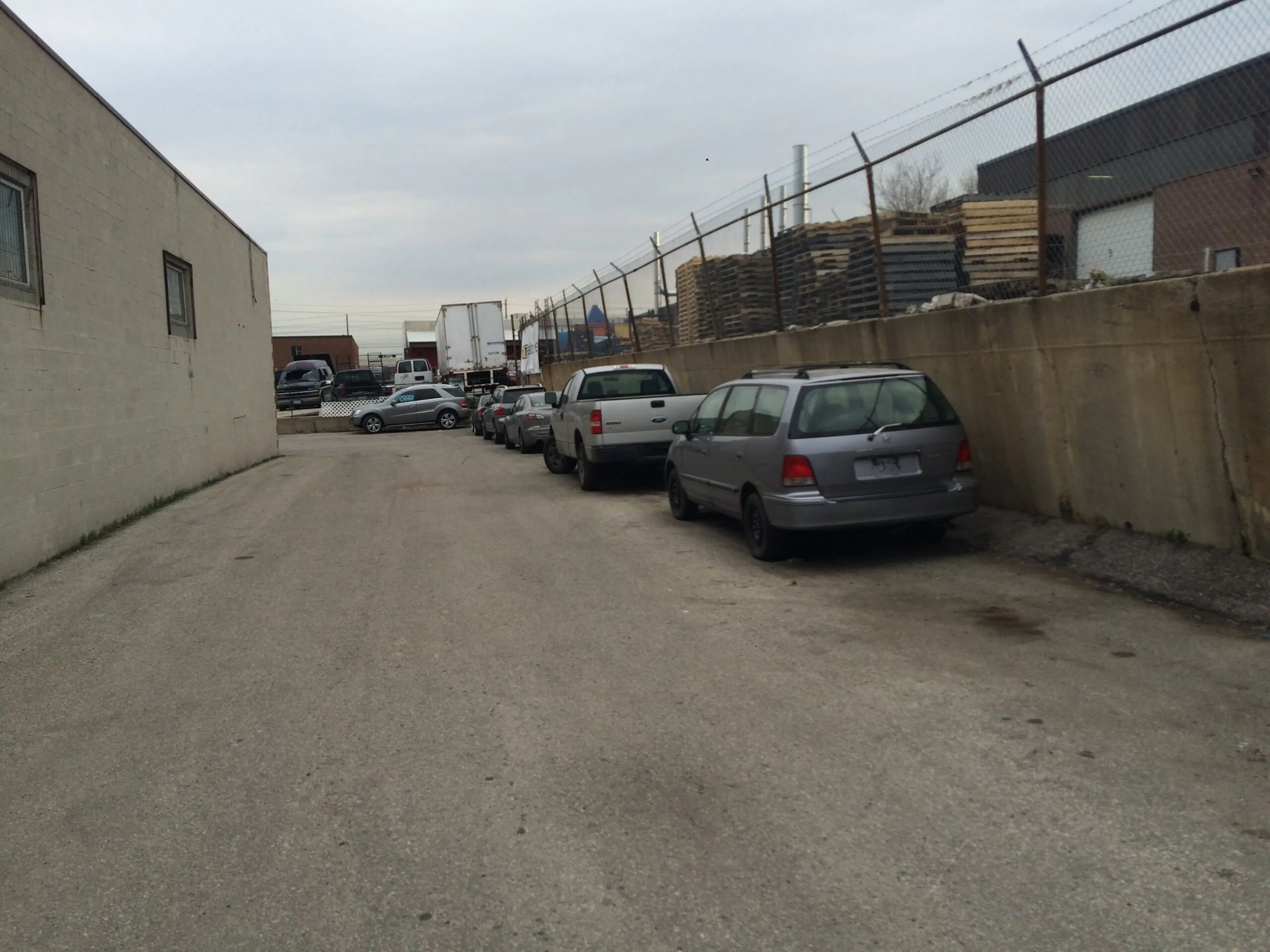 Narrow service lane at the Smokey Manufacturing plant before construction, cars parked below the failing concrete retaining wall