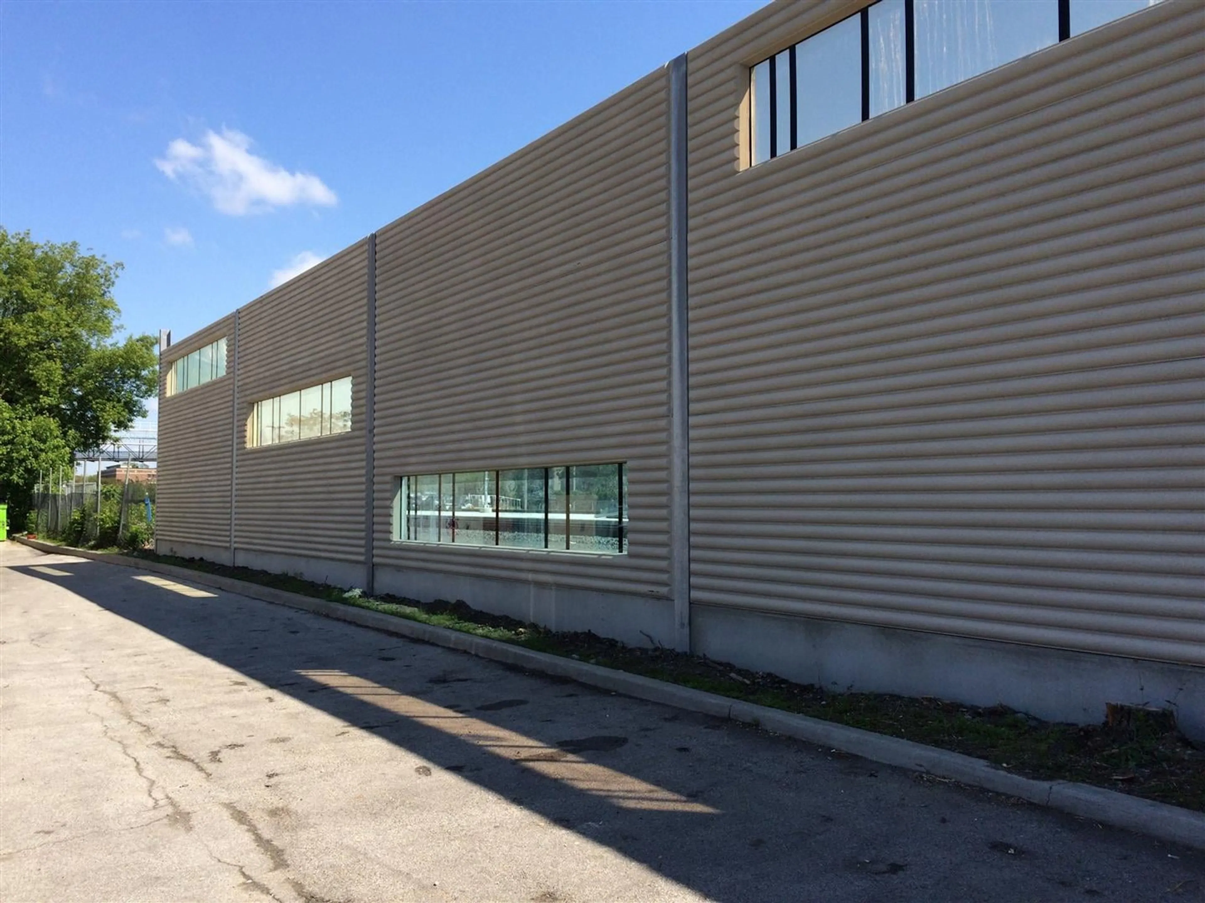 Long horizontally ribbed precast screen wall running beside a paved lane on the UP Express corridor