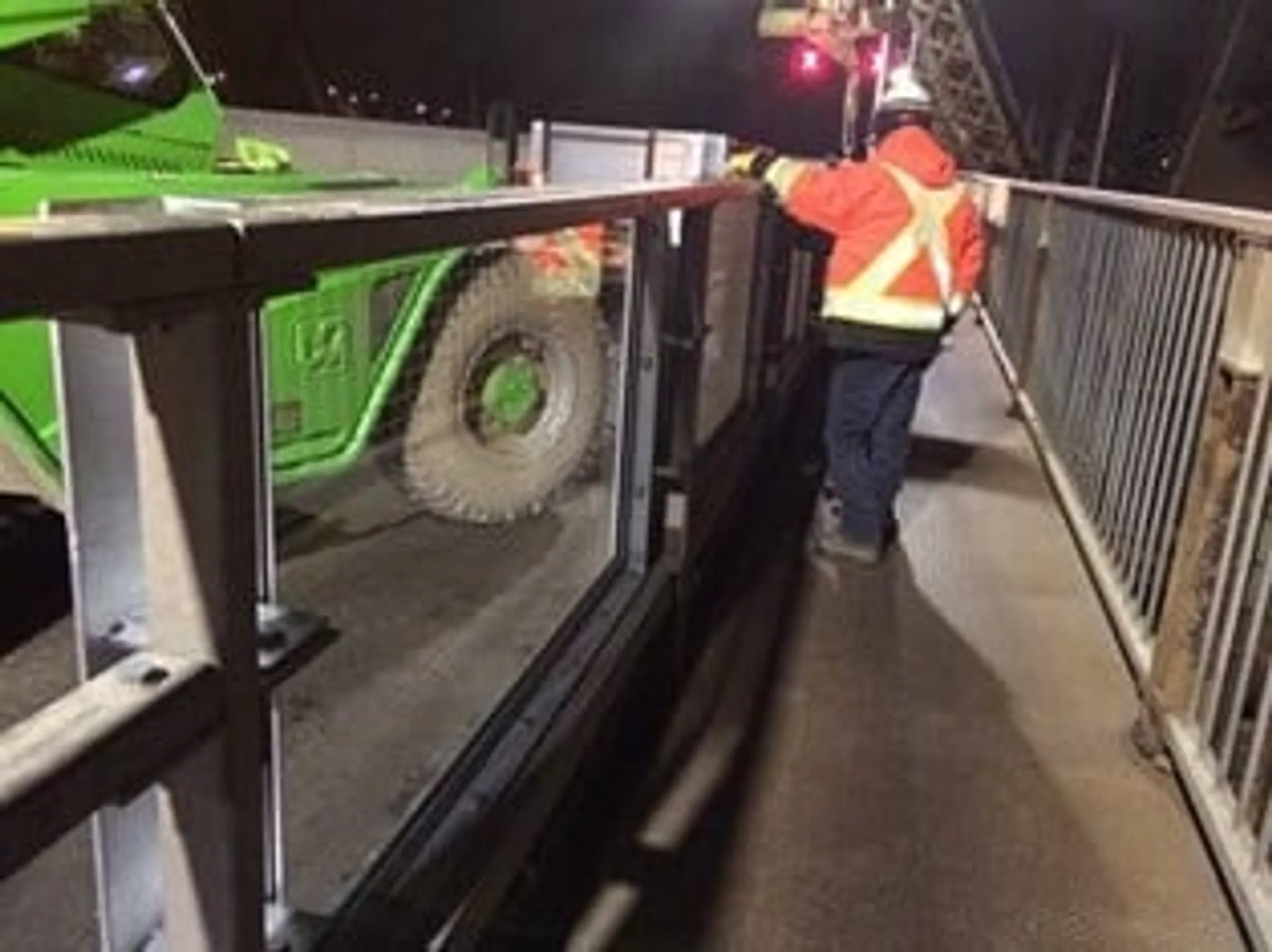 Night work on the Pont de Quebec: a worker in high-visibility gear on the deck beside a loader and the new panelled barrier