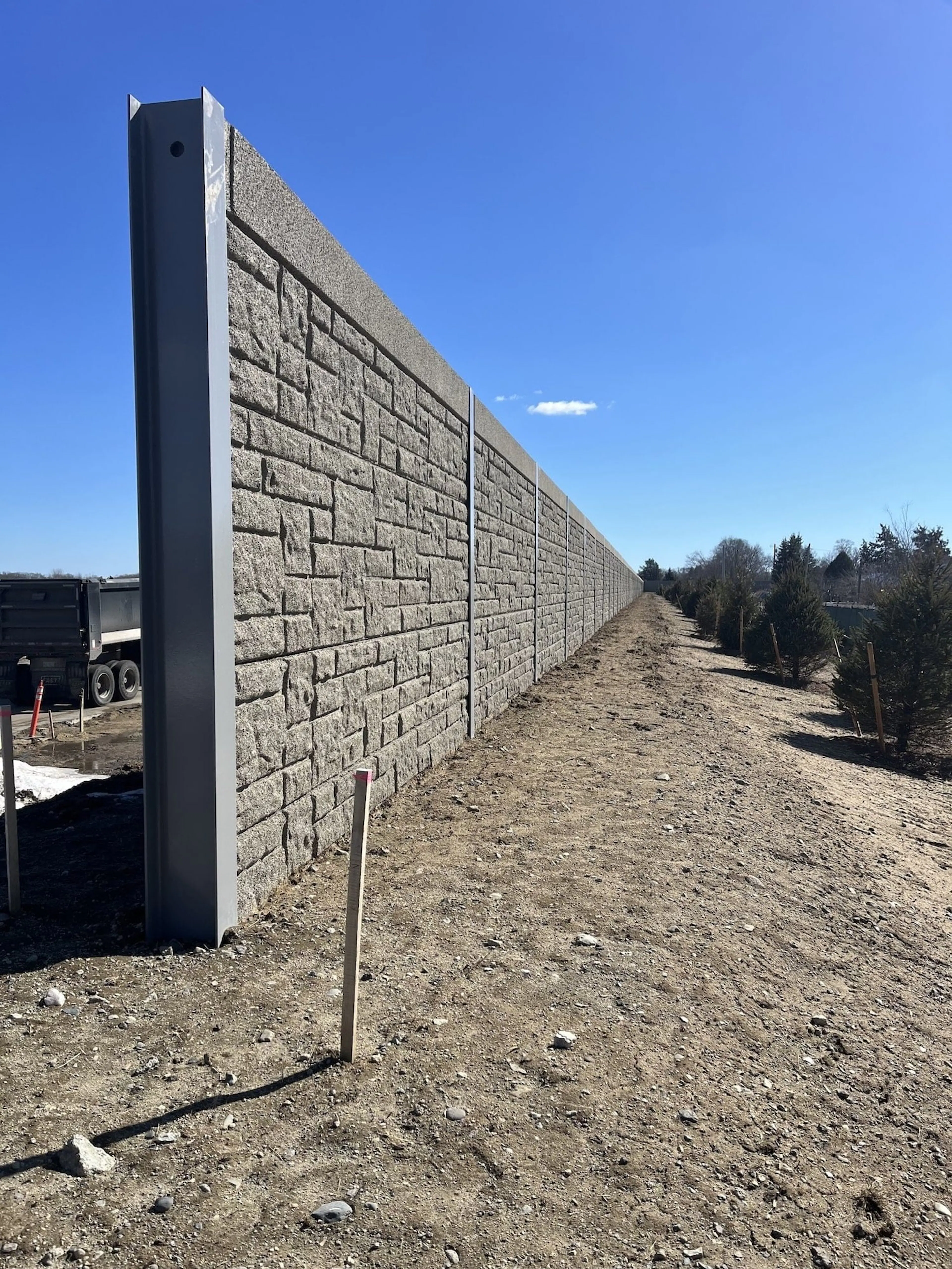 Stone-textured sound wall receding into the distance, with a steel end post in the foreground
