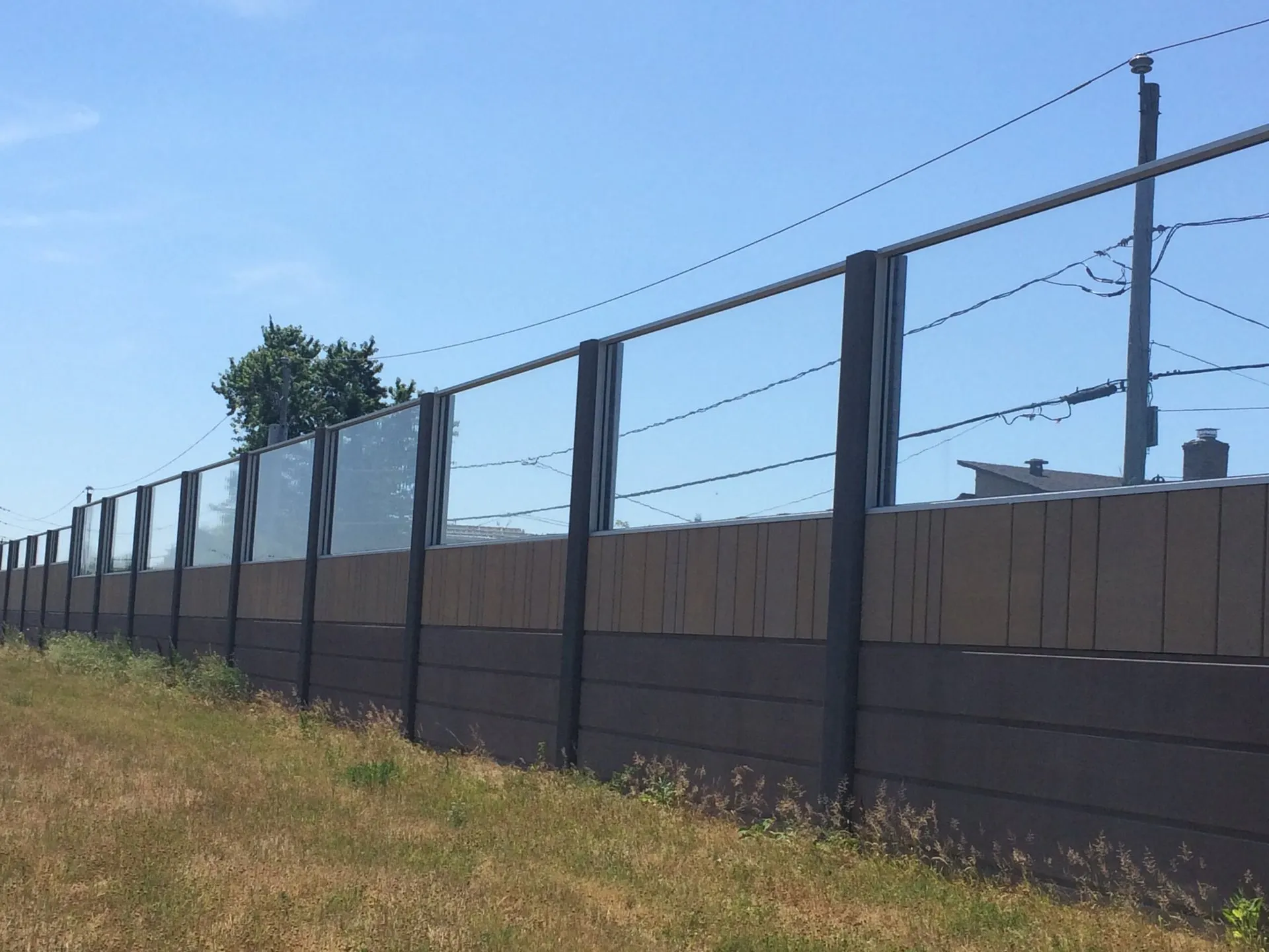 Noise wall with clear transparent panels above the absorptive base, alongside a grassed shoulder