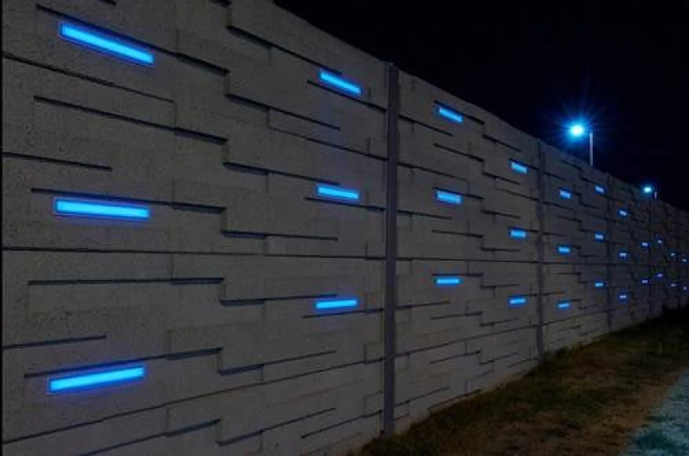 Precast noise wall at the OC Transpo garage lit at night by blue LEDs recessed into its staggered block pattern
