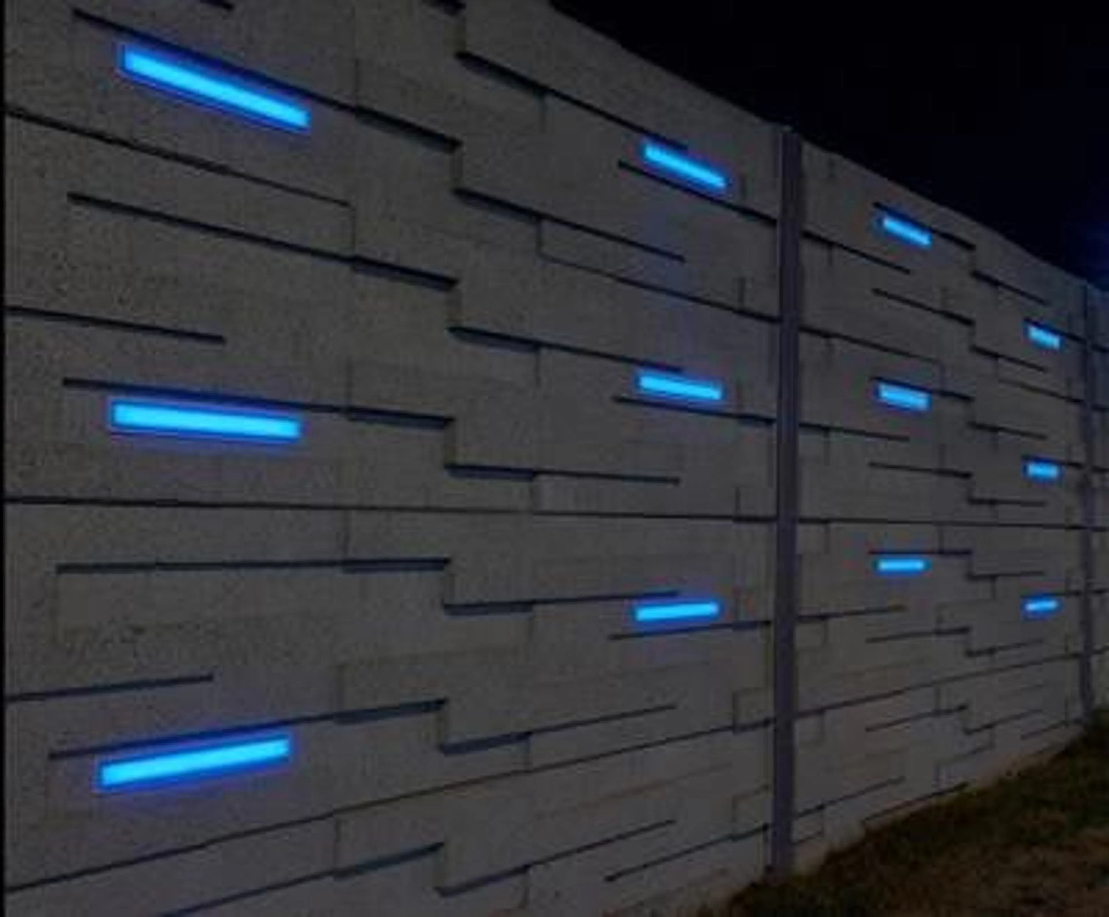 Precast noise wall at the OC Transpo garage lit at night by blue LEDs recessed into its staggered block pattern
