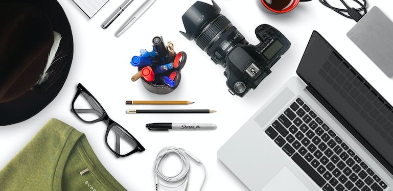Ordinateur portable, appareil photo, lunettes, stylos et vêtements sur une table de bureau