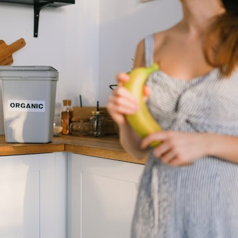 Femme tenant une banane devant un bac à compost