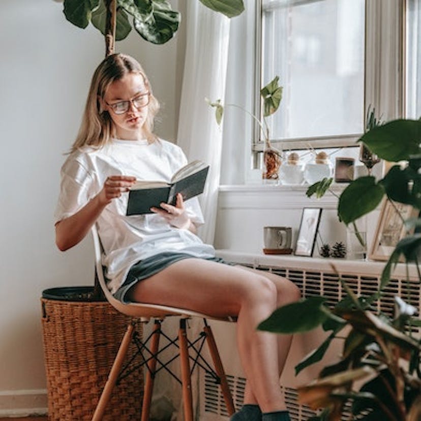 femme qui lit à côté d'un radiateur avec une tête thermostatique connecté et des plantes vertes