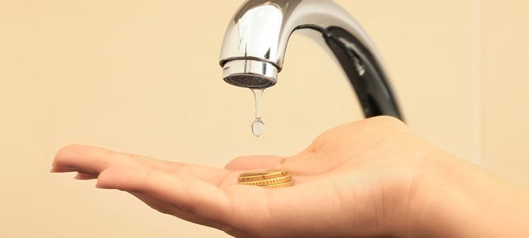 Un robinet d'eau coulant sur des pièce de monnaie tenues par une main humaine