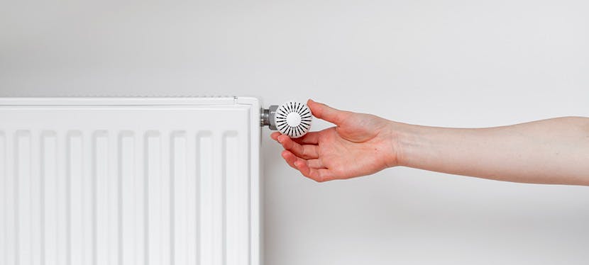 Une main qui tourne le thermostat d'un radiateur : quand éteindre le chauffage ?