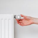 Une main qui tourne le thermostat d'un radiateur : quand éteindre le chauffage ?