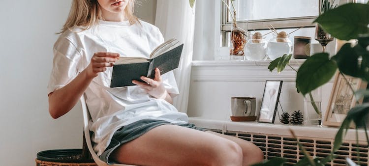 femme qui lit à côté d'un radiateur avec une tête thermostatique connecté et des plantes vertes