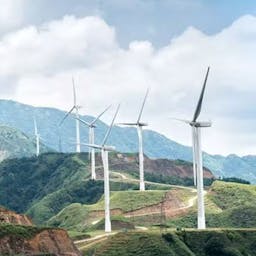 Des éoliennes blanches le long d'une route de montagne participant à la transition écologique.