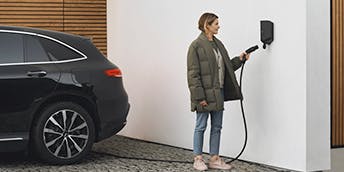 Une femme qui branche sa voiture électrique sur sa borne de recharge installée à domicile