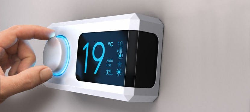 Une main tourne le bouton d'un thermostat pour faire des économies d'énergie.