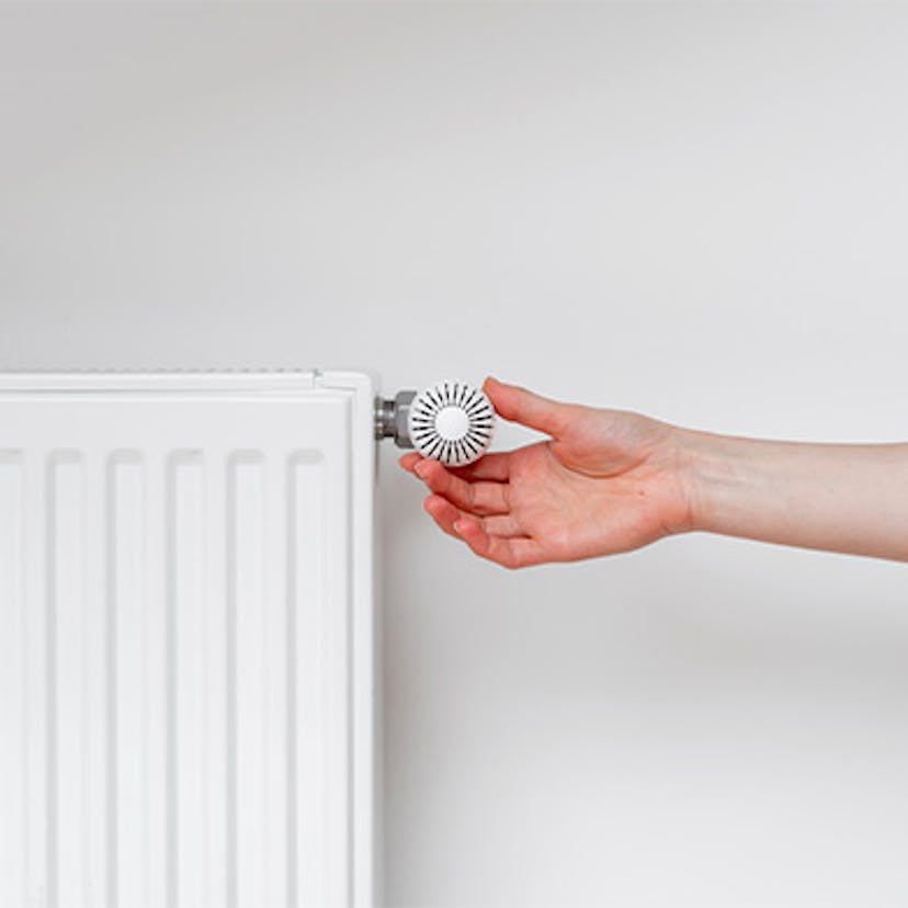 Une main qui tourne le thermostat d'un radiateur : quand éteindre le chauffage ?