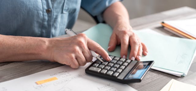 Personne qui calcule la consommation de ses appareils électriques à l'aide d'une calculatrice