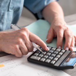 Personne qui calcule la consommation de ses appareils électriques à l'aide d'une calculatrice