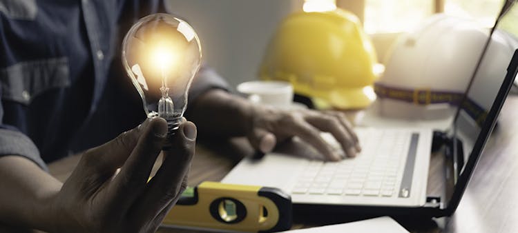 Un homme devant un ordinateur tenant une ampoule électrique