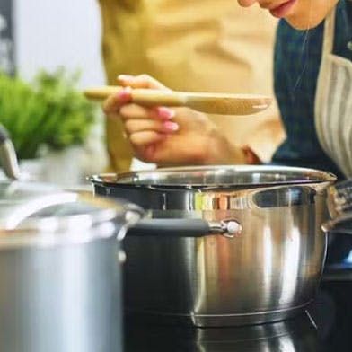 Une femme en train de cuisiner, penchée au-dessus d'une marmite.