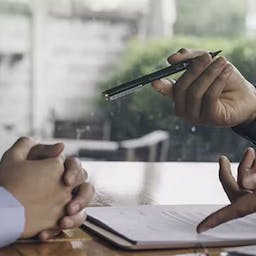 Une personne montrant un contrat et tendant un stylo à une autre personne
