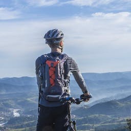 Un homme tenant son vélo éléctrique et regardant le paysage.