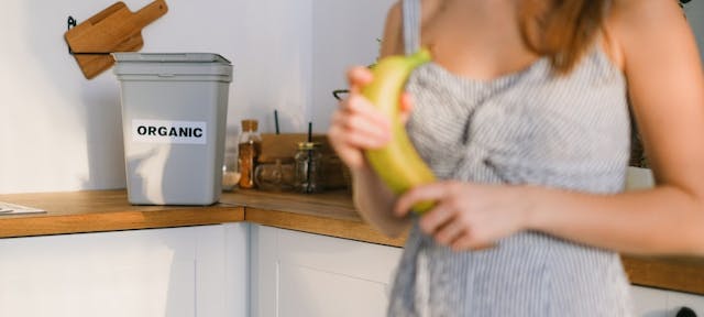 Femme tenant une banane devant un bac à compost