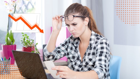 A woman looking closely at a computer with a frown. A chart with a downward trajectory.