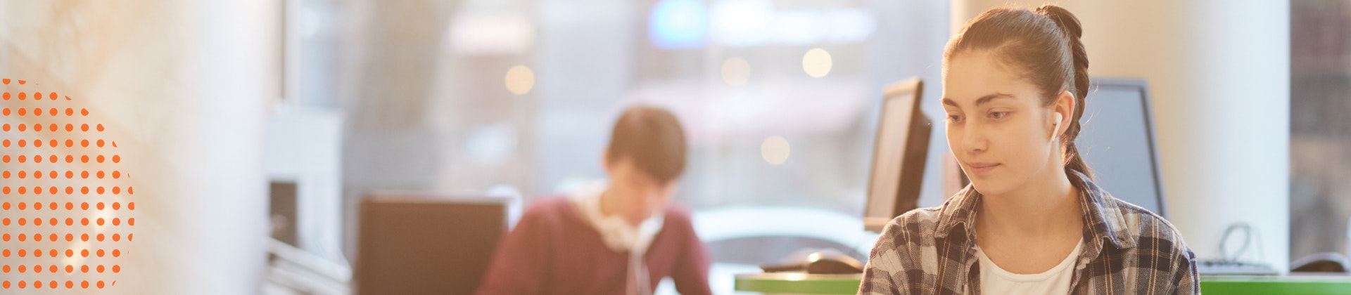 Young white female with brown hair sitting at a laptop computer with a notebook in hand.