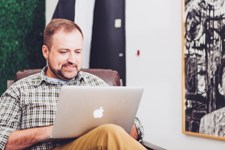 A photo of a man sitting in a chair and looking at his laptop