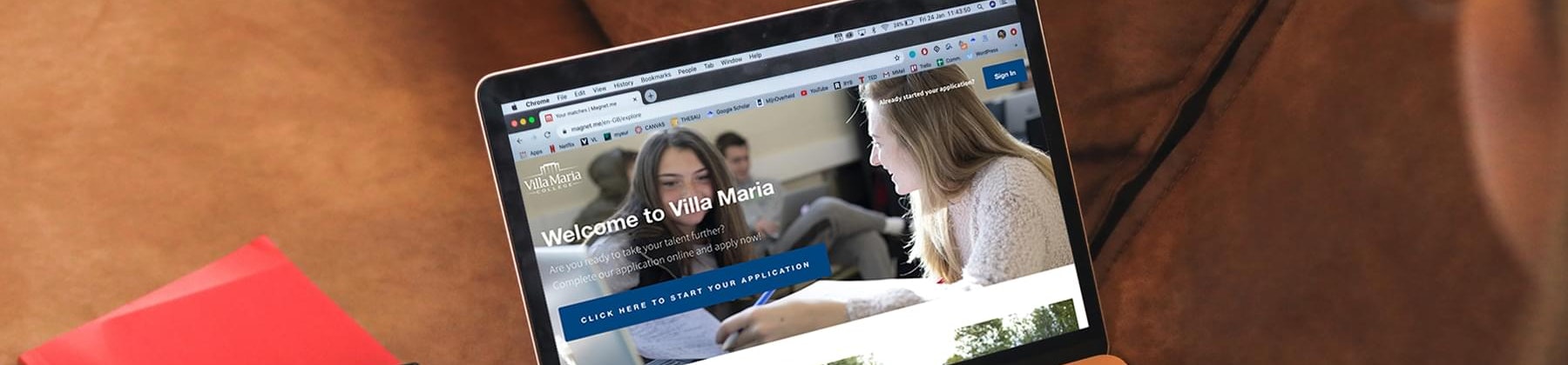 Picture of a woman browsing the Villa Maria website on her laptop, and having a red notebook next to her on the sofa.