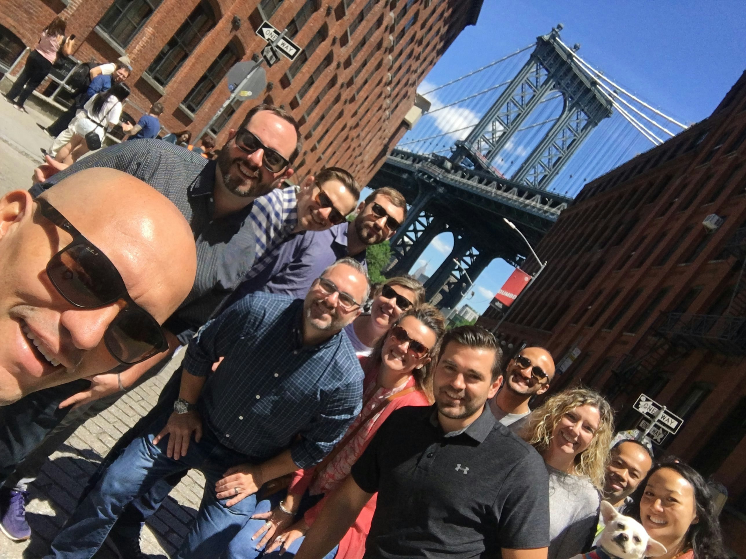 A group of people stand in the street posing under the Brooklyn Bridge.