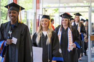Smiling Georgia Highlands College graduates in caps and gowns walking in a commencement processional