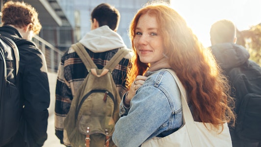 Girl college student walking behind a group of other students and looking behind her.
