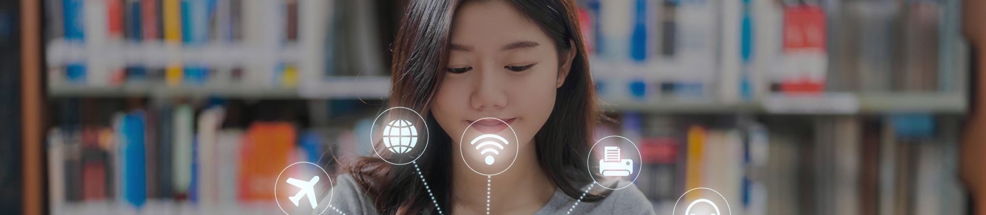 College Student sitting at a table in the library looking at a book with AI icons over top of the book.