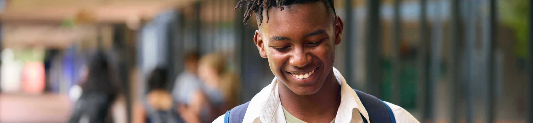 Student walking and smiling down at phone in hand.