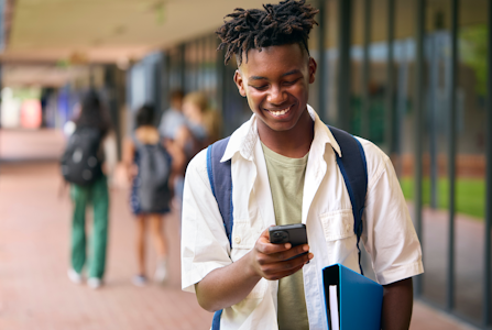 Student walking and smiling down at phone in hand.