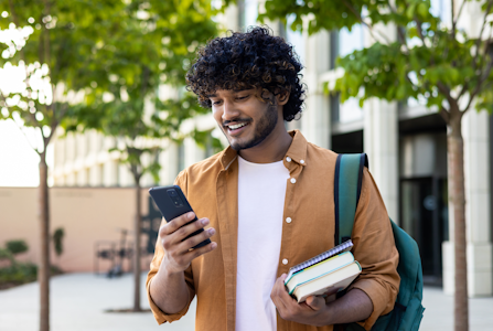 College student looking down at his phone and smiling.