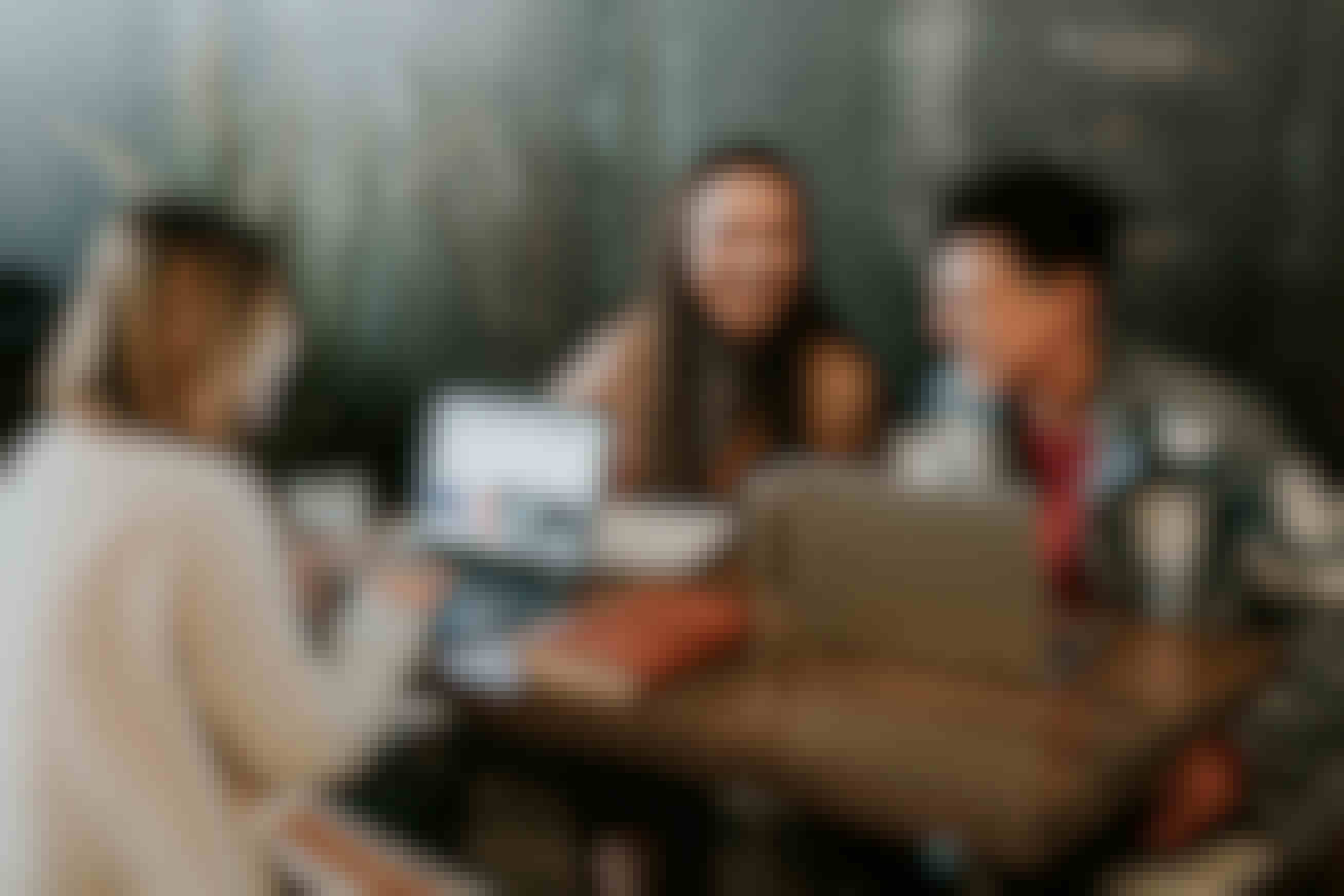 An image of three students at a work table on their laptops laughing