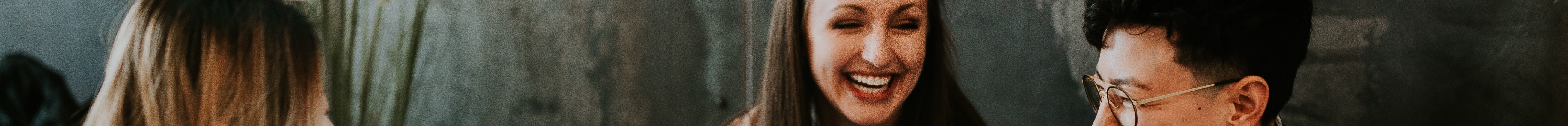 An image of three students at a work table on their laptops laughing