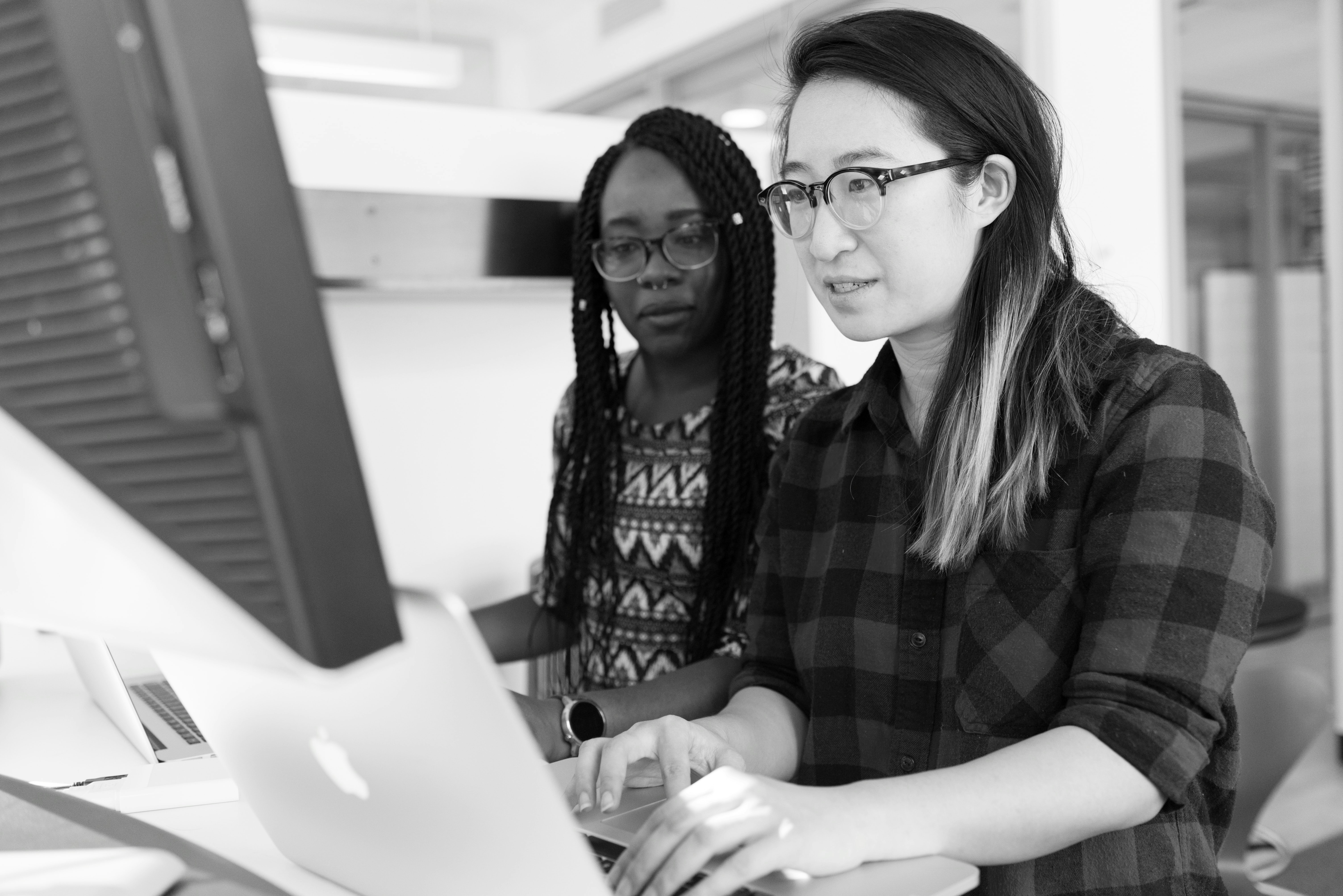 Two women working together at a standing desk on their laptops