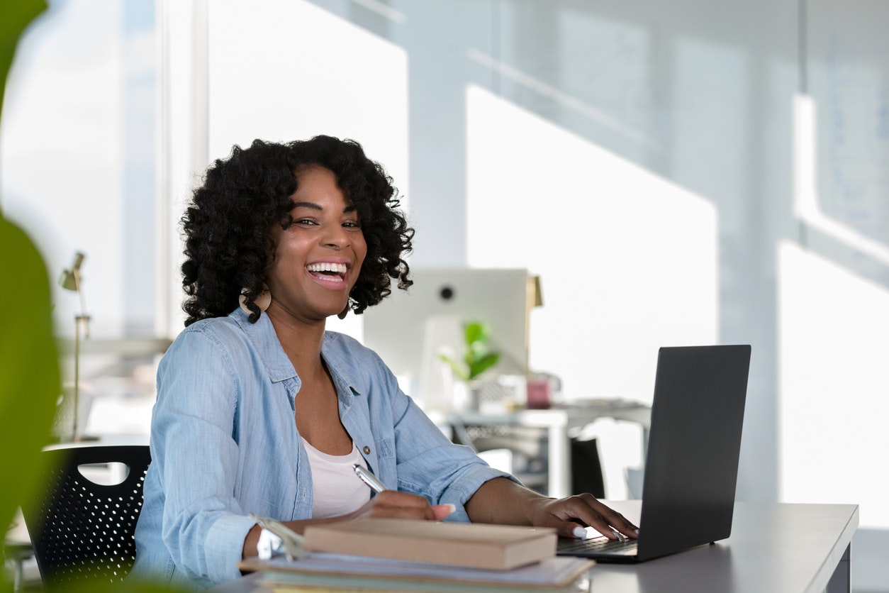 A female staff member working and smiling at her computer.