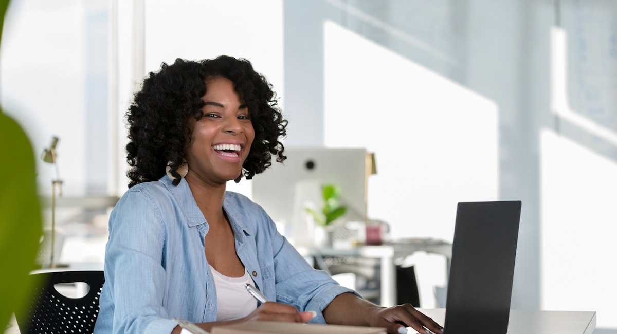 A female staff member working and smiling at her computer.