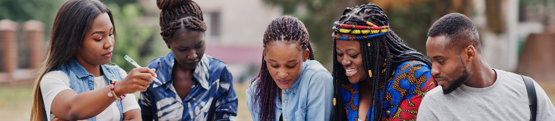A group of students sitting on the grass, looking at a computer screen and smiling.