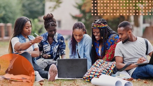 A group of students sitting on the grass, looking at a computer screen and smiling.