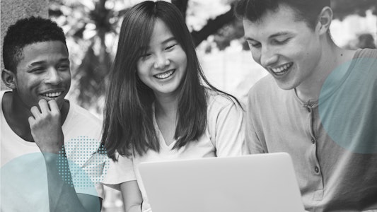 Three students are looking at a laptop and laughing.